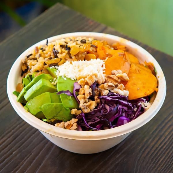 A Sprout Mediterranean salad bowl with avocado, purple cabbage, walnuts, rice, and sweet potatoes.